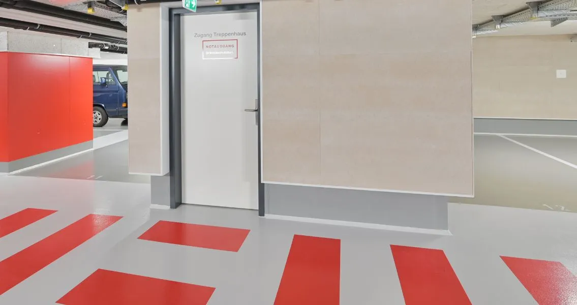 Die Pfeiler und Bodenmarkierungen in der Tiefgarage sind in einem kraftvollen RAL-Ton 3016, einem tiefen Korallenrot, gehalten.