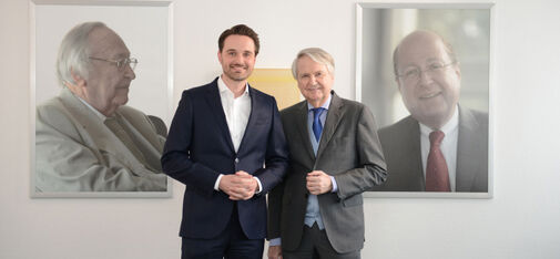 Drei Generationen der Unternehmerfamilie Müller: Dr. Claus-M. Müller mit seinem Sohn Nicolaus vor den Porträts seines Vaters und Firmengründers Heinrich W. Müller (links; †2010) und seines Bruders Dr. Bertram R. Müller (†2012).